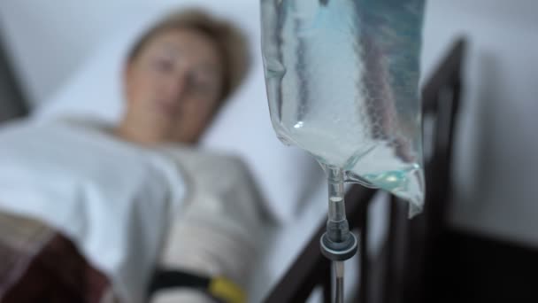 Капельница, стоящая на фоне слабого пожилого пациента, спящего в больничной палате, терапия — стоковое видео