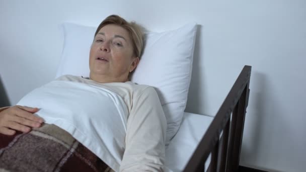 Nemocný starší ženský pacient ležící na ošetřené posteli, stěží dýchá a žádá o pomoc — Stock video