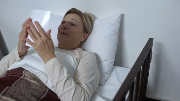 Отчаянная больная женщина лежит на больничной койке, смотрит на семейное фото и плачет — стоковое видео