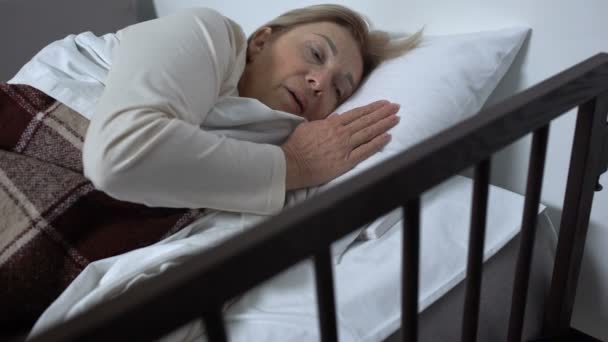 Зріла пацієнтка лежить в лікарняному ліжку, відчуває нудоту і натискає кнопку виклику — стокове відео