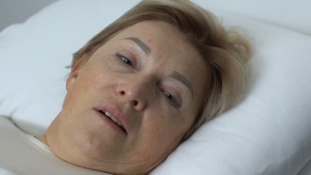 Femme âgée déçue couchée au lit, face fermée avec une main tremblante, crise — Video