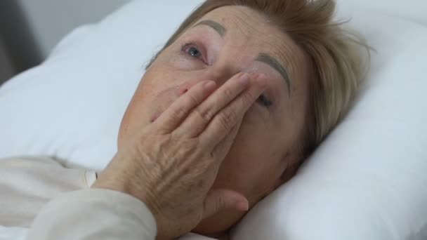 Плачущая пожилая женщина лежит в постели дома, депрессия, жизнь и проблемы со здоровьем — стоковое видео
