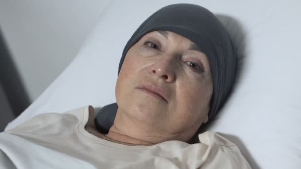 Mujer de edad trastornada en bufanda acostada en la cama y mirando a la cámara, paciente de quimioterapia — Vídeos de Stock