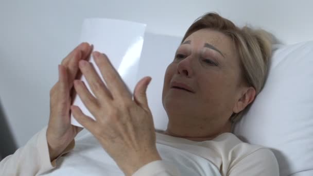 Плаче старша жінка лежить у ліжку і дивиться на фото, пам'ятаючи чоловіка — стокове відео