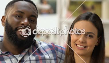 Düz kanepede oturan büyük kağıt kalp gösteren çekici çok etnik çift