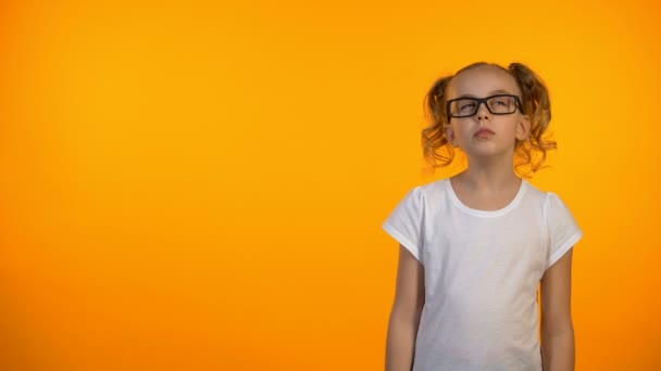 Маленькая гениальная девочка, поднимающая палец на оранжевом фоне, имея идею — стоковое видео