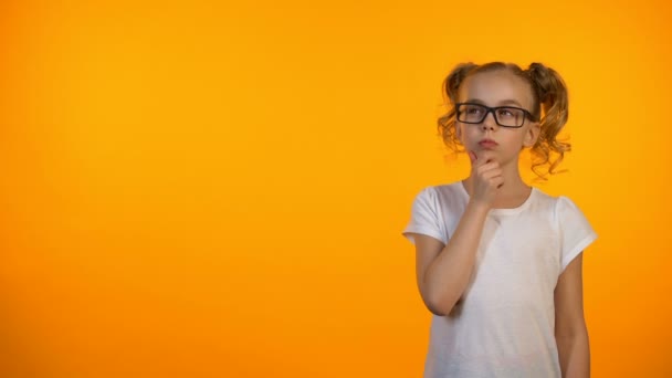 Penive Preteen meisje denken geïsoleerd op oranje achtergrond, planning onderwijs — Stockvideo