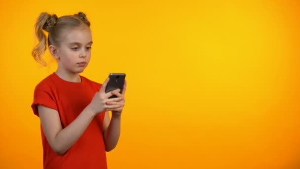 Sonriente niña escribiendo en el teléfono inteligente y sonriendo, aplicación educativa, gadget — Vídeos de Stock