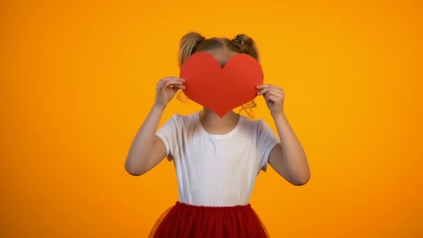 Mooi meisje verstopt achter rood papier hart, glimlachend naar de camera, Valentijnsdag, liefde — Stockvideo