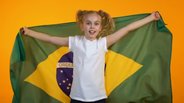 Adorable niña preadolescente saltando con bandera brasileña animando a su equipo favorito — Vídeo de stock