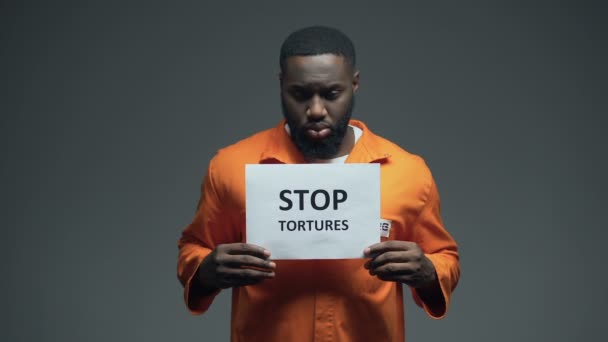 Μαύρος κρατούμενος που κρατάει την πινακίδα "Σταμάτα τα βασανιστήρια", κακομεταχείριση βίας — Αρχείο Βίντεο