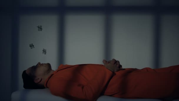 Кавказский заключенный лежит и думает на доске в камере, отбывая пожизненное заключение — стоковое видео