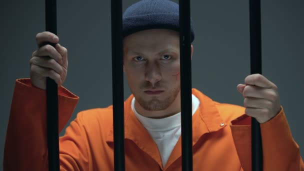 Caucasian male prisoner with scar on face holding bars and looking directly — Stock Video