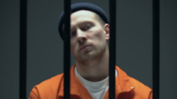 Dangerous arrogant prisoner standing behind bars and showing handcuffed hands — Stock Video