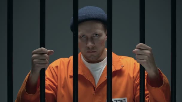 Агрессивный опасный заключенный мужчина со шрамом на лице, держащий решетки и кричащий — стоковое видео