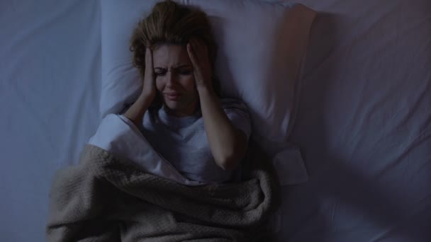 Girl holding head lying in bed, trying to fall asleep in bustling area of city — Stock Video