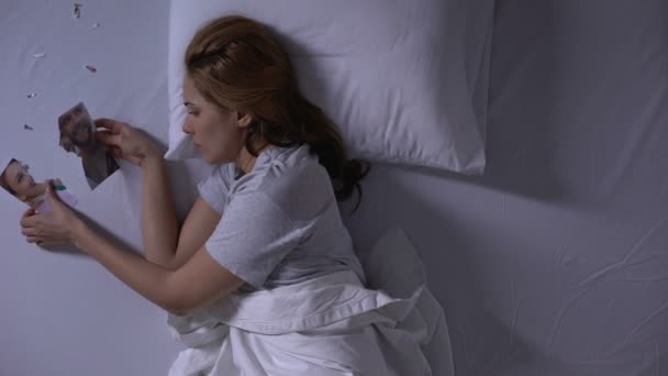 Dziewczyna leżąca w łóżku patrząc na łzawienie zdjęcie swojego chłopaka, twarde break-up — Wideo stockowe