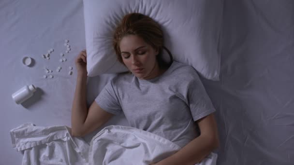 Jovem mulher pacificamente deitada na cama perto do frasco aberto com pílulas, overdose, suicídio — Vídeo de Stock