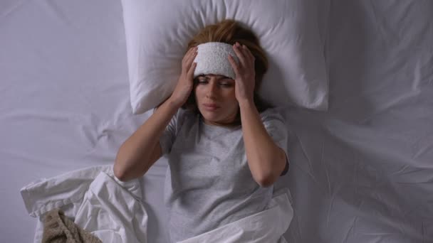 Magas lázban szenvedő fiatal nő, fekve az ágyban borogatással a homlokán — Stock videók