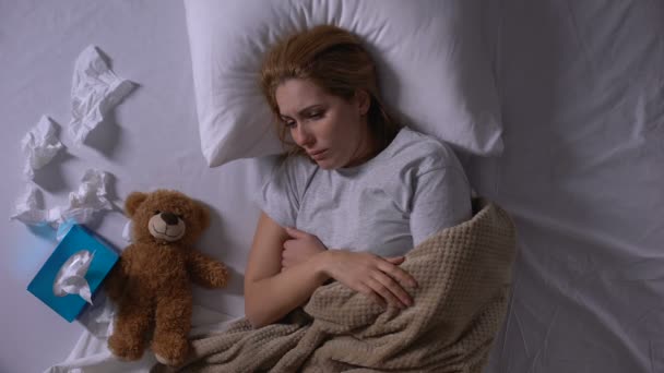 Депресивна жінка в ліжку плаче, обіймає плюшевого ведмедя, страждає від викидня — стокове відео