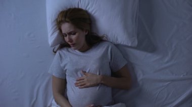 Yalnız bekleyen kadın yatakta göbek okşayarak ağlıyor, umutsuzluk, depresyon