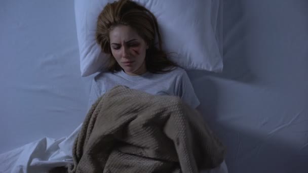 Λυπημένη κυρία με τραύμα στο πρόσωπο κλαίγοντας στο κρεβάτι τη νύχτα καλύπτοντας με κουβέρτα, κατάχρηση — Αρχείο Βίντεο