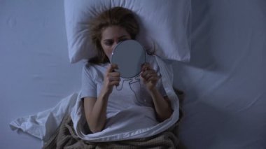 Yüzünde yara olan üzgün kadın yatakta yatan aynaya bakıyor, aile içi şiddet