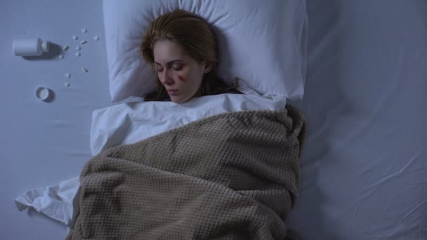 Medvetslös sårad kvinna liggande i sängen uppifrån, piller nära kudde, självmord — Stockvideo