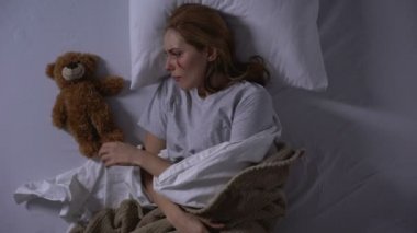 Kadın şiddet kurbanı oyuncak ayı oyuncak sarılma, yatakta ağlama, acı duygular