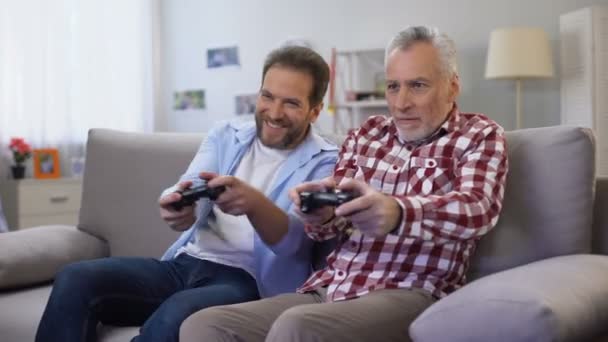 Взрослый отец и сын играют в видеоигры, веселятся вместе, развлекаются — стоковое видео
