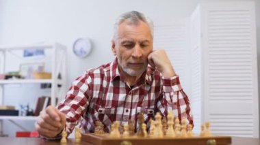Yaşlı erkek tek başına satranç oynuyor ve kameraya bakıyor yarışmaya hazırlanıyor