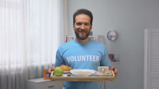 Volontario maschio sorridente di mezza età che mostra vassoio con colazione alla macchina fotografica, cura — Video Stock