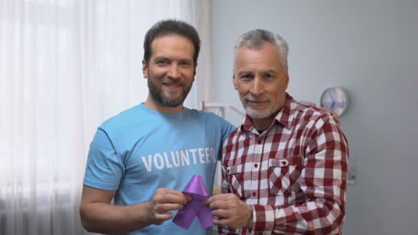 Voluntario y hombre mayor mostrando cinta púrpura, conciencia de la enfermedad de Alzheimer — Vídeo de stock