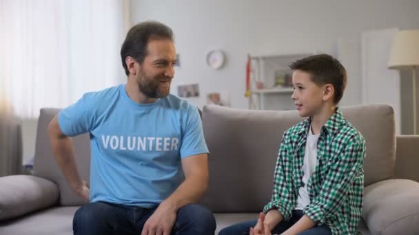 Un bénévole souriant attentif donne un ballon de football orphelin, les rêves se réalisent — Video