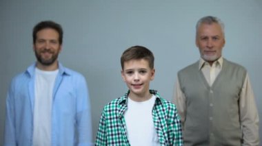 Kameraya bakan genç çocuk, arka planda orta yaşlı ve yaşlı erkekler, destek