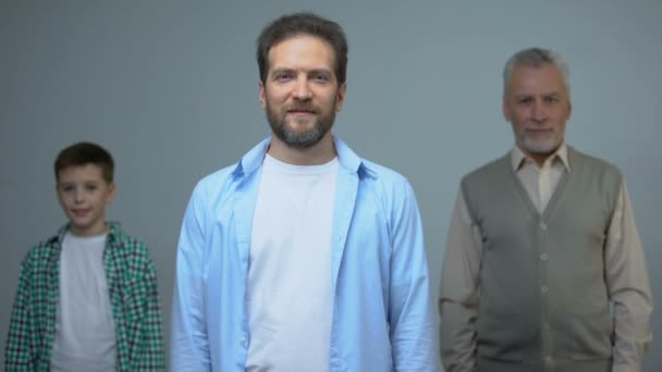 Hombre de mediana edad sonriendo a la cámara, hombre y niño mayor detrás, pasado y futuro — Vídeos de Stock