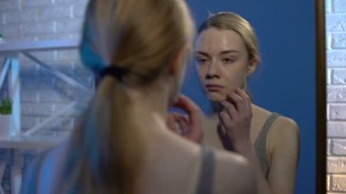 Ağlayan genç evde aynaya bakarak sorun yüz cilt inceleyerek, akne