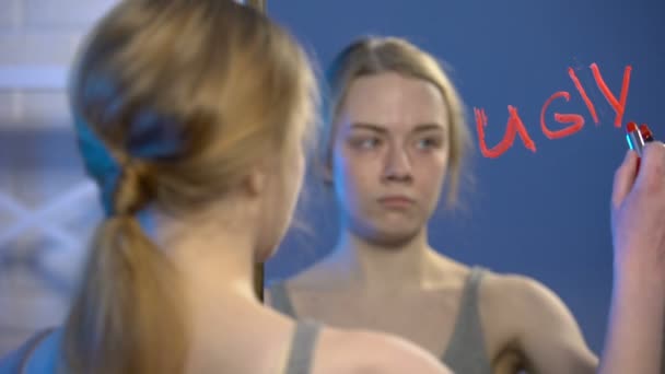 Unhappy teenager writing word ugly by lipstick on mirror, puberty insecurities — Stock Video