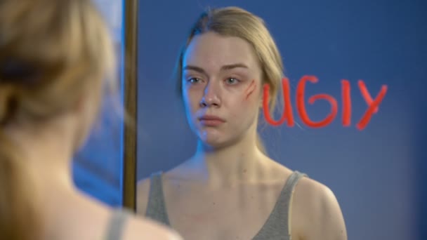 Triste jeune femme avec blessure sur le visage pleurer, mot laid écrit sur verre miroir — Video