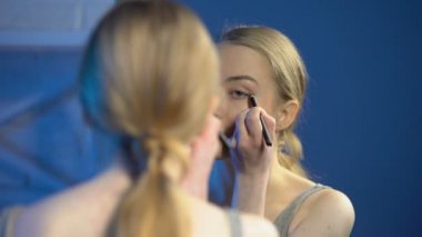 Aynanın önünde eyeliner uygulayan güzel genç kadın, makyaj yapmayı öğreniyor