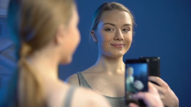 Oyuncu genç yüzler yapıyor, aynanın önünde akıllı telefonla selfie çekiyor — Stok video