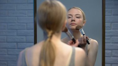 Aynanın ön yüz pudrası uygulayan çekici genç kadın, kamera karşısında gülümseyerek