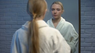 Genç bir kadın göbeğini okşayıp aynaya bakıyor, genç bir kız bekliyor.