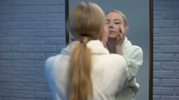 Hermosa mujer en albornoz aplicando crema facial hidratante, belleza natural — Vídeo de stock