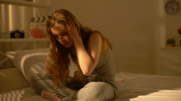 Беспокойная женщина сидит дома на кровати, навязчивые мысли, нервозность, проблемы — стоковое видео