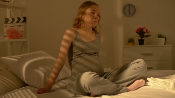 Отчаянно ожидая, что женщина прикоснется к животу сидя на кровати, беременность трудности — стоковое видео