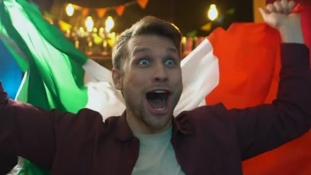 Abanico extremadamente alegre ondeando bandera italiana en el bar, regocijando la victoria de la selección nacional — Vídeo de stock