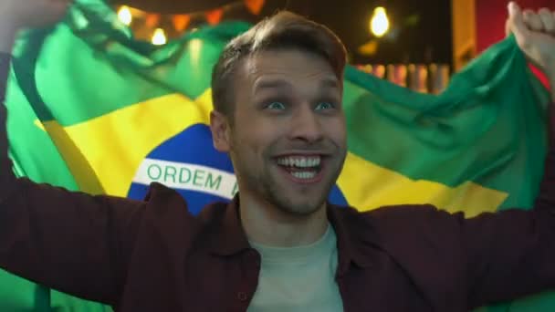 Збуджена чоловічий вентилятор розмахуючи Бразильський прапор в барі, веселі спортивна команда перемога — стокове відео