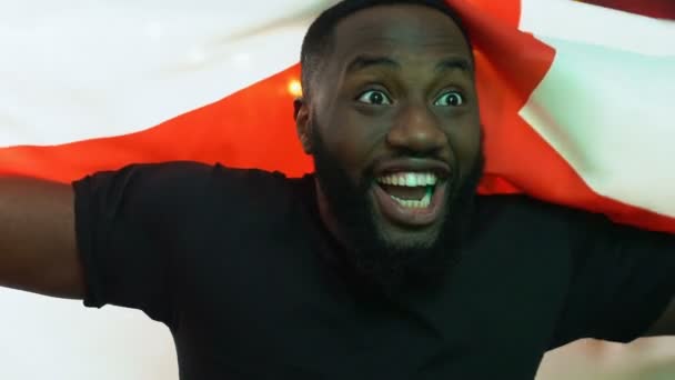 Vzrušený černý fanoušek mávající anglickou vlajkou, raduje se z vítězství národního sportovního týmu — Stock video
