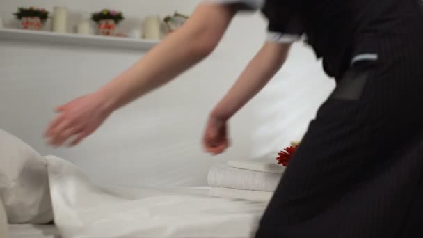 Молодая горничная застилает постель в гостиничном номере, кладет цветы, заботится о клиентах — стоковое видео